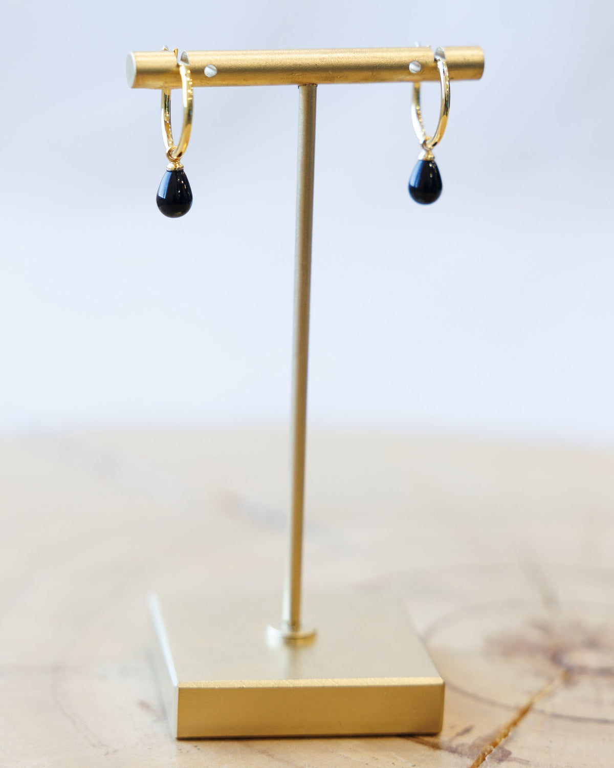 Gold earring stand with black teardrop earrings on a light background