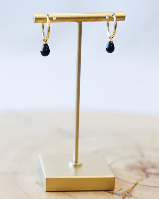 Gold earring stand with black teardrop earrings on a light background