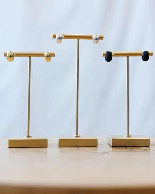 Three gold jewelry display stands on a light wooden surface with a white background