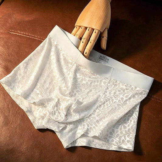 White patterned briefs with a wide elastic waistband, displayed on a brown leather surface with a wooden mannequin hand holding the waistband.