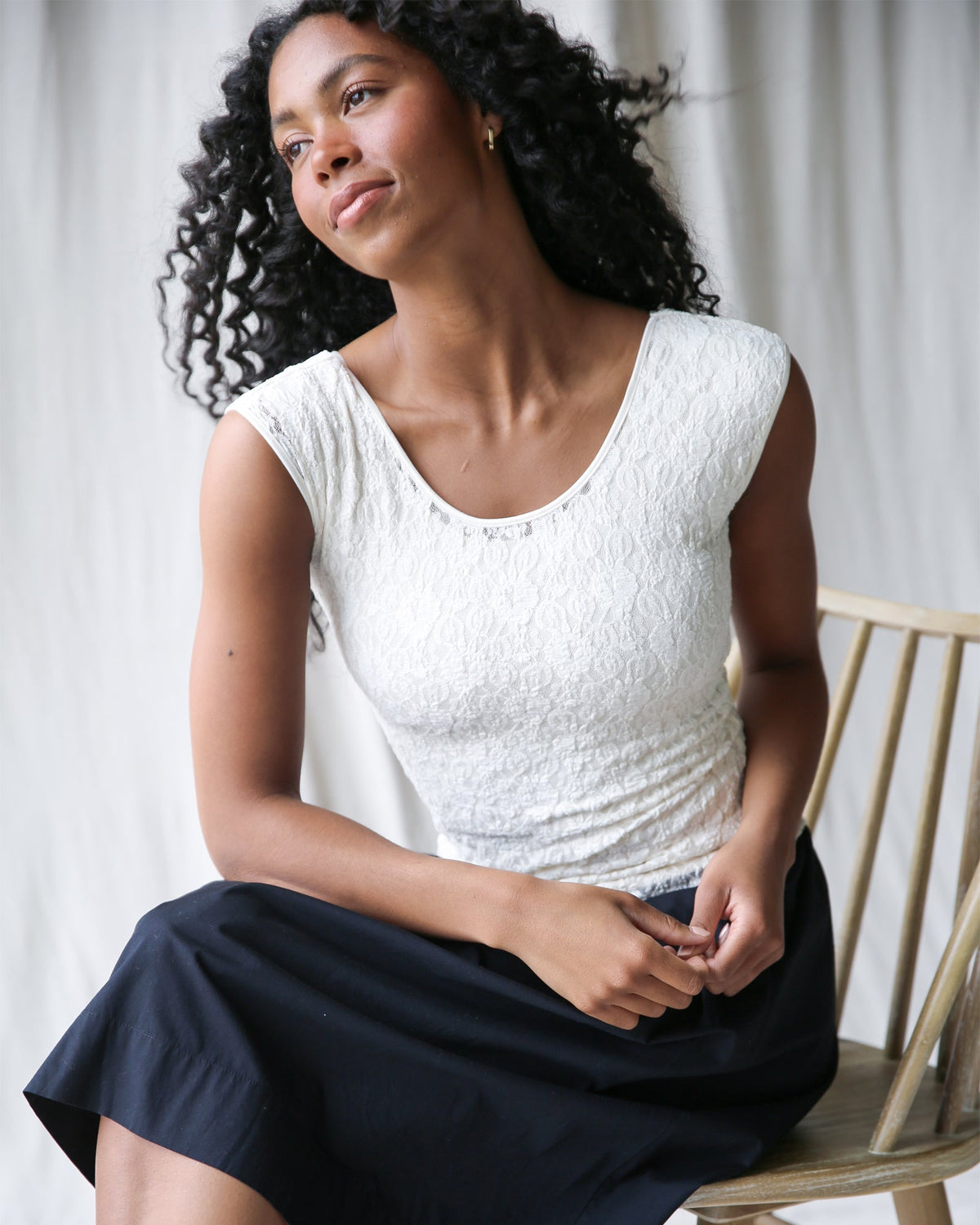 Woman wearing a white top and navy skirt sitting on a wooden chair.