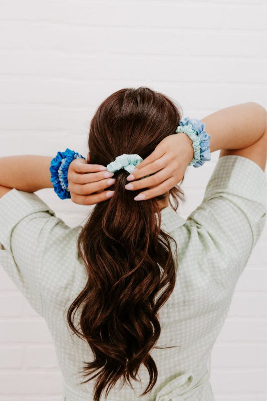 Person with long hair wearing multiple scrunchies on a light background