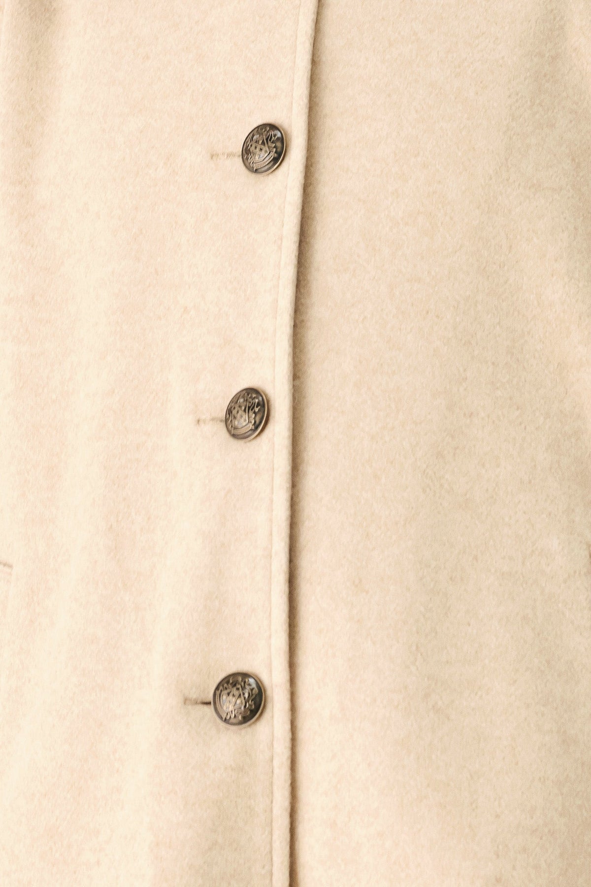 Close-up of a cream-colored textured fabric garment with a vertical button placket and four dark metal buttons.
