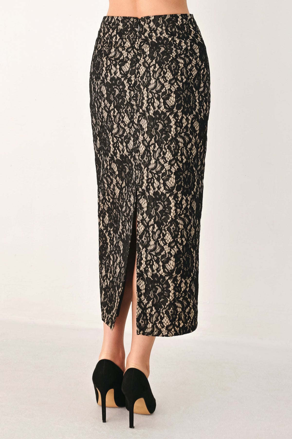 A black lace midi skirt with a front slit, shown on a model from the waist down wearing black high heels against a plain light background.