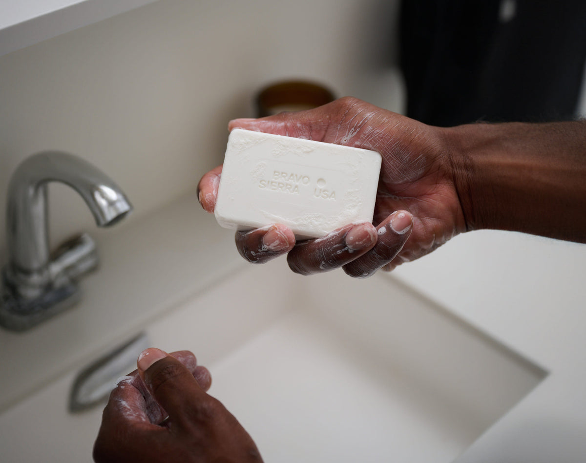 Person holding a bar of soap above a sink with a faucet in the background