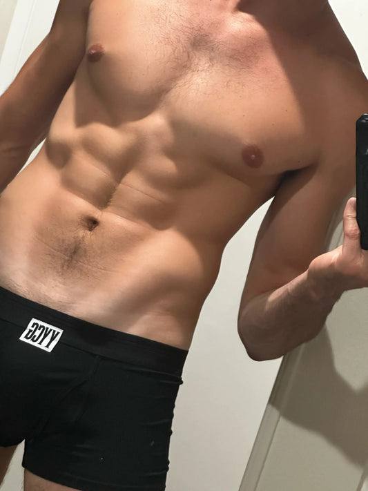 Man wearing black boxer briefs with a brand logo, taking a mirror selfie.