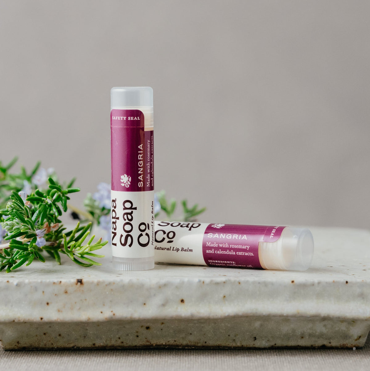 Two lip balms from Napa Soap Co on a stone surface with greenery in the background
