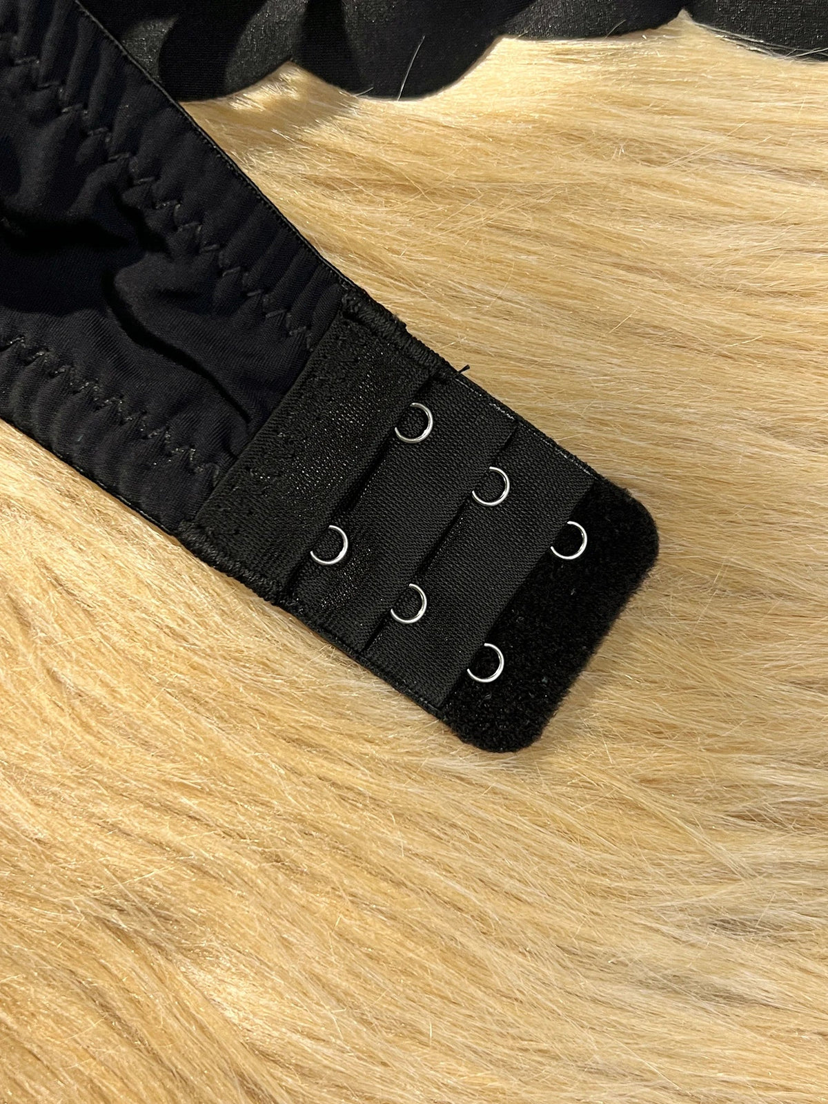 Close-up of a black adjustable strap with three metal grommets and a hook-and-loop closure, laid on a beige faux-fur surface.
