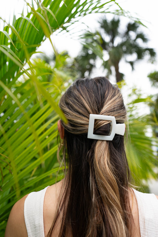 Person with a hair clip in a ponytail against a green leafy background