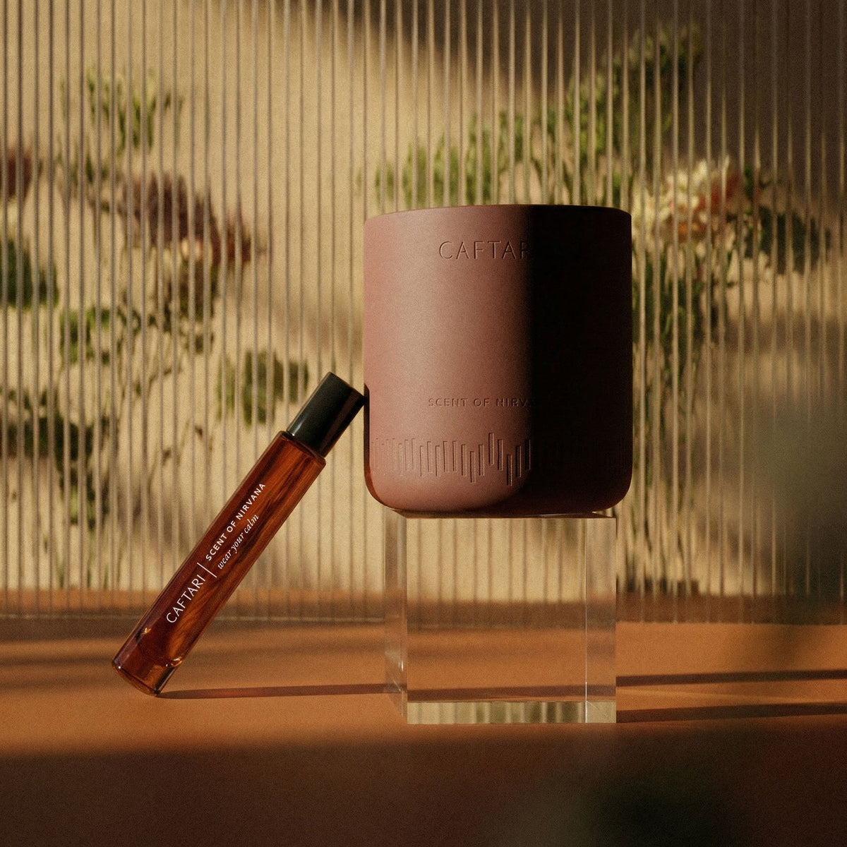 Brown candle and rollerball on a clear stand with blurred greenery in the background