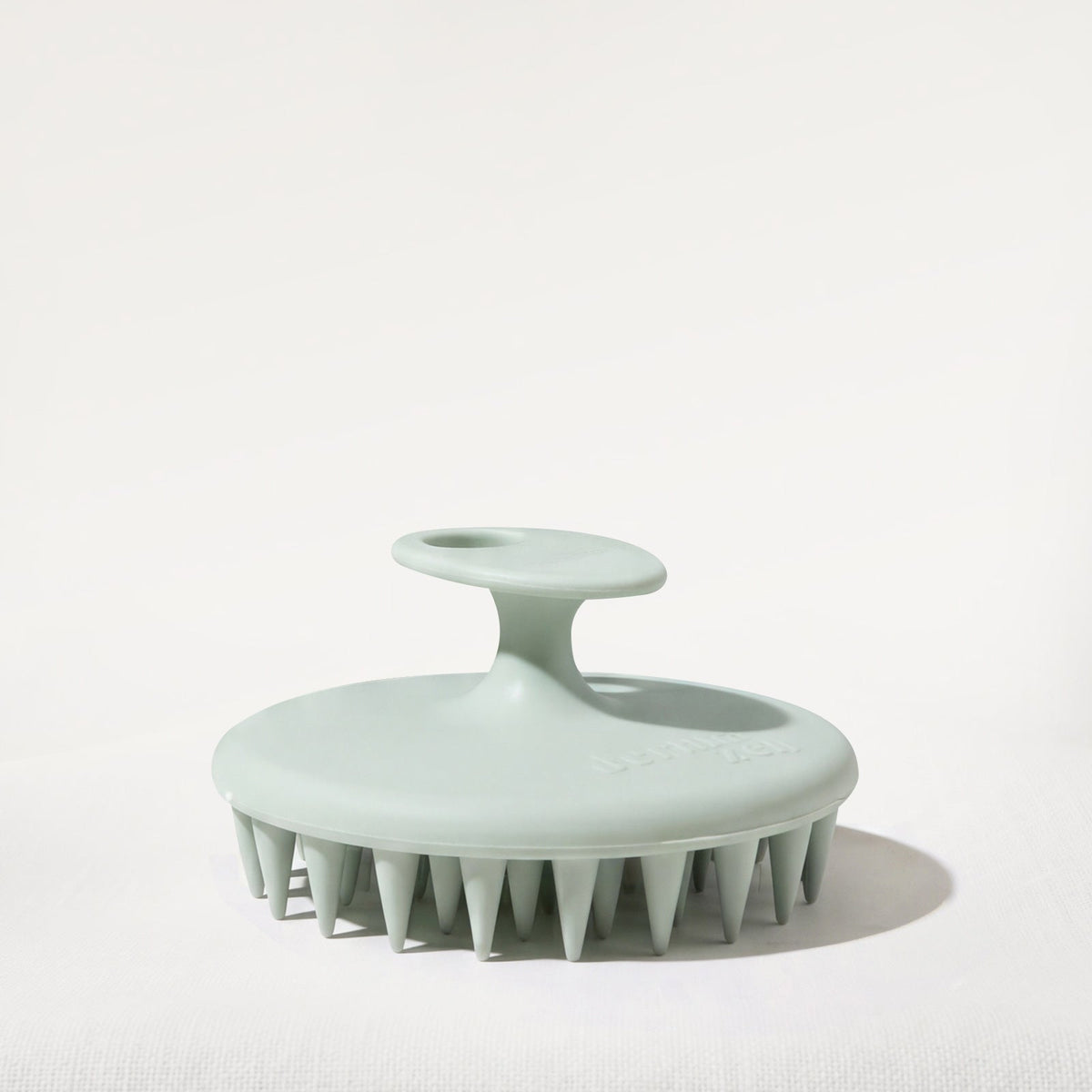 Light green scalp massage brush on a white background