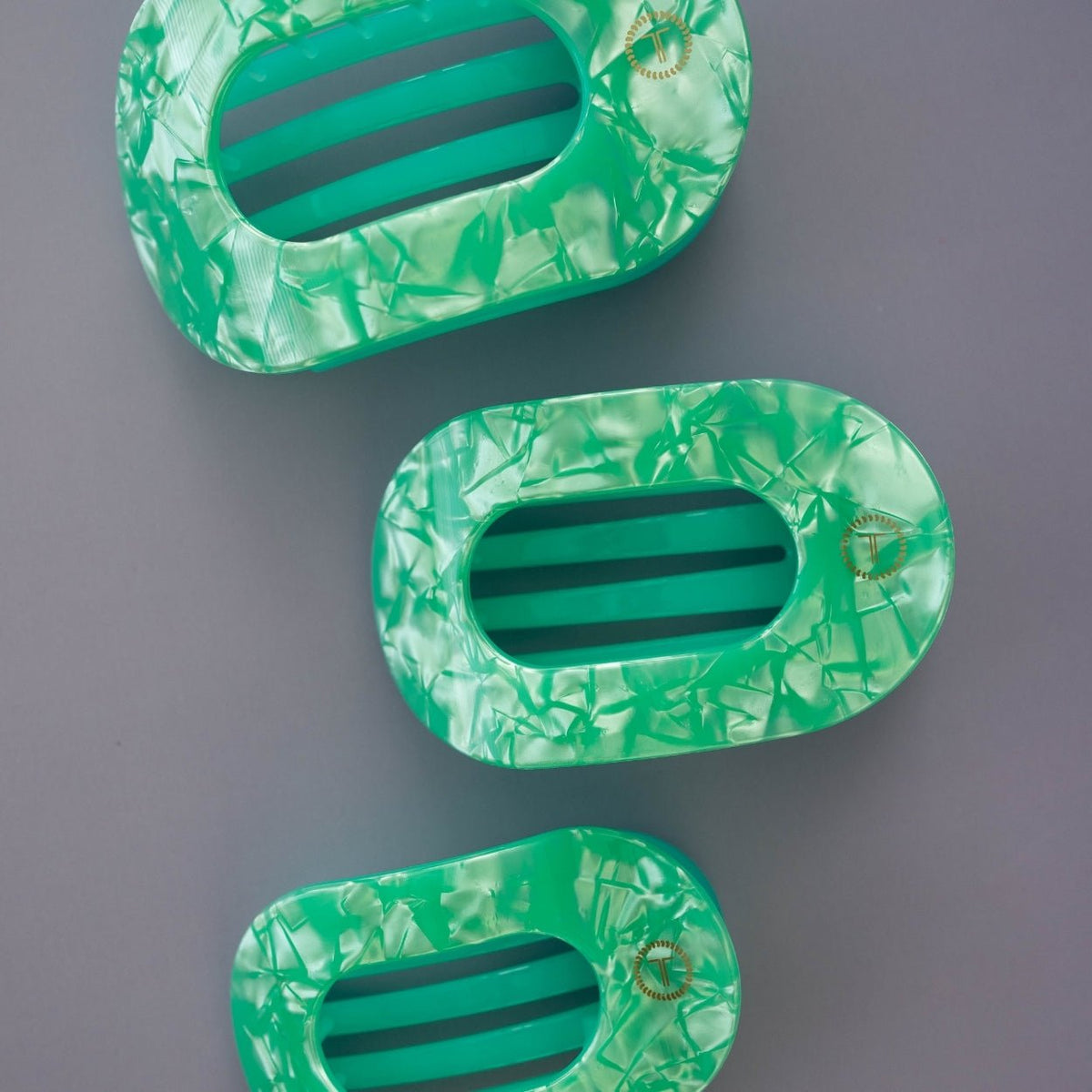 Three green marbled hair clips on a gray background