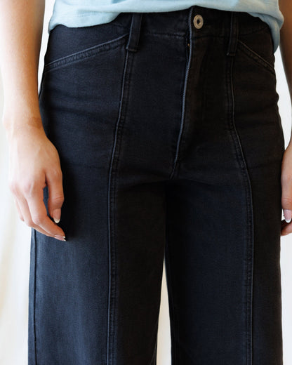 Close-up of a person wearing dark washed denim jeans with a light blue top partially visible at the waist.