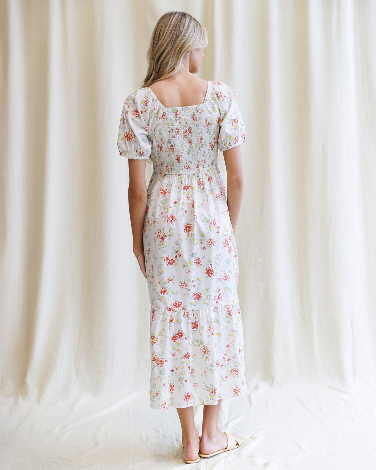 Woman wearing a floral dress standing against a white curtain