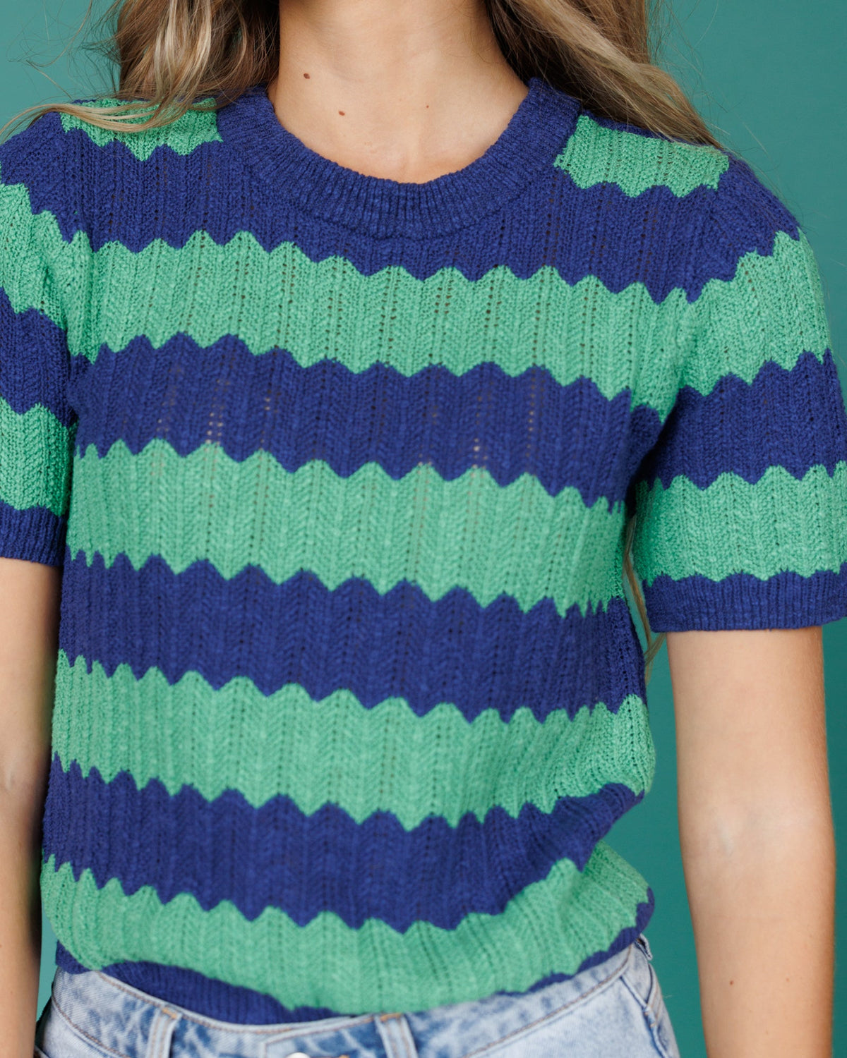 Green and blue striped sweater worn by a person on a teal background