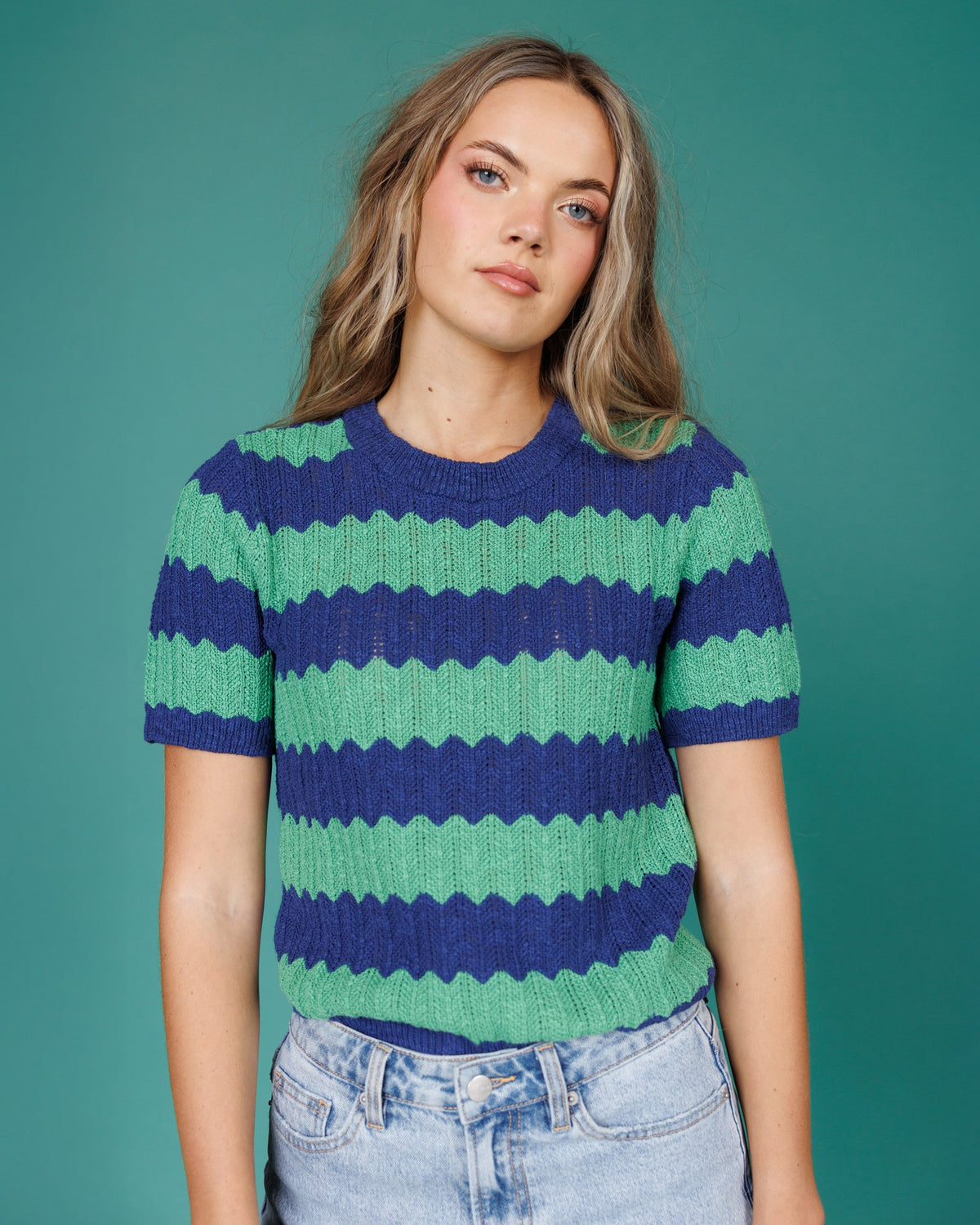 Person wearing a blue and green striped sweater against a teal background