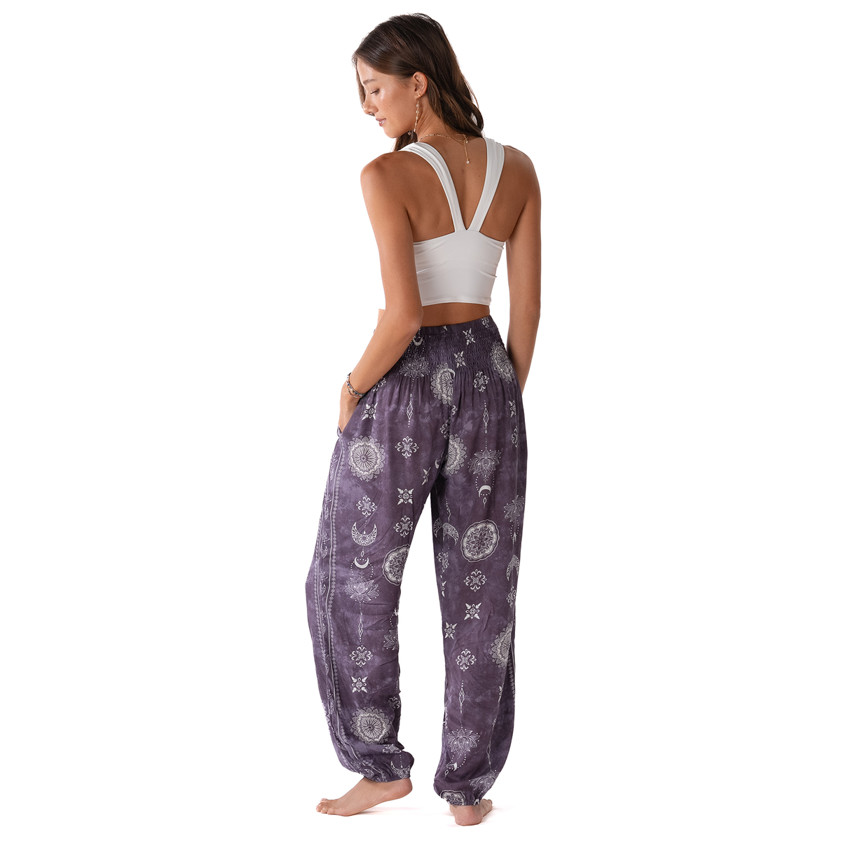 Woman wearing a white sports bra and purple patterned pants on a white background