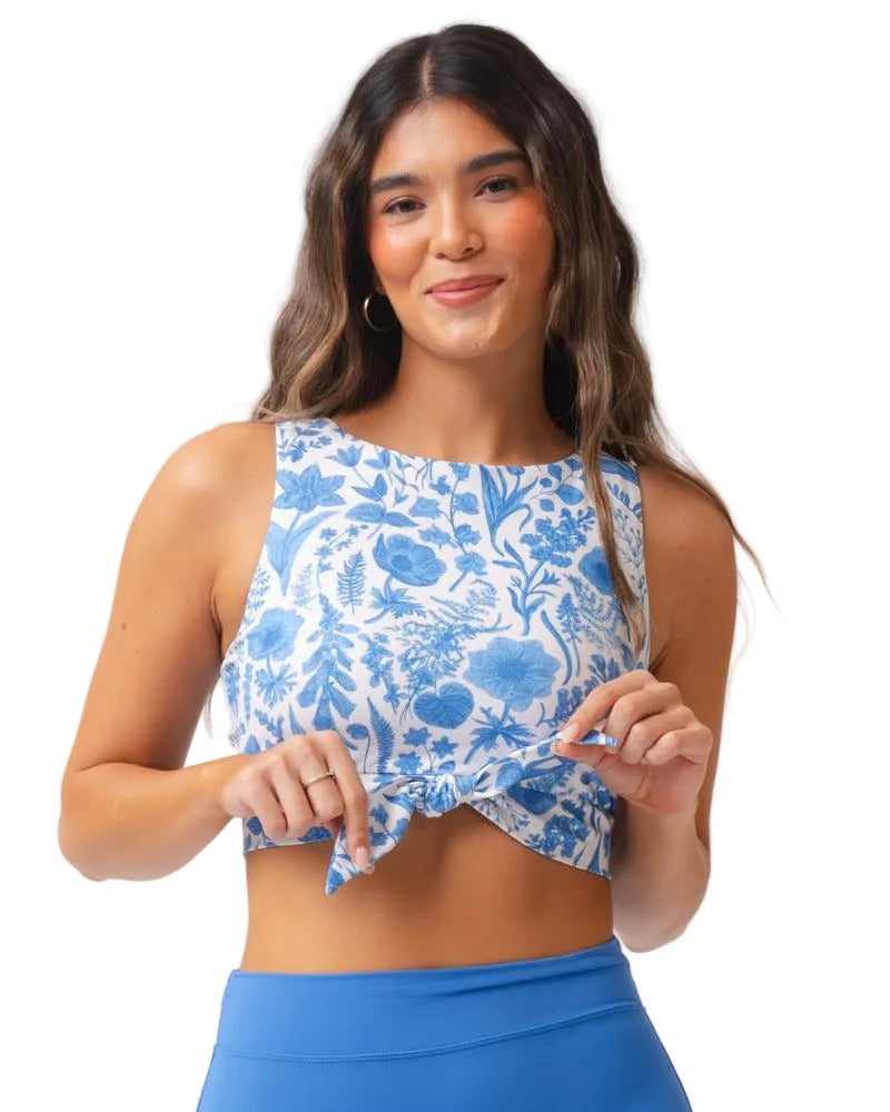 A woman modeling a sleeveless crop top with a blue and white floral toile pattern, paired with blue athletic bottoms, against a solid white background.