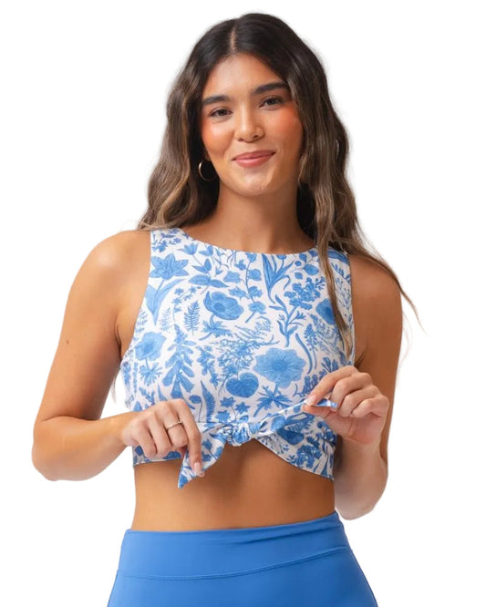 A woman modeling a sleeveless crop top with a blue and white floral toile pattern, paired with blue athletic bottoms, against a solid white background.