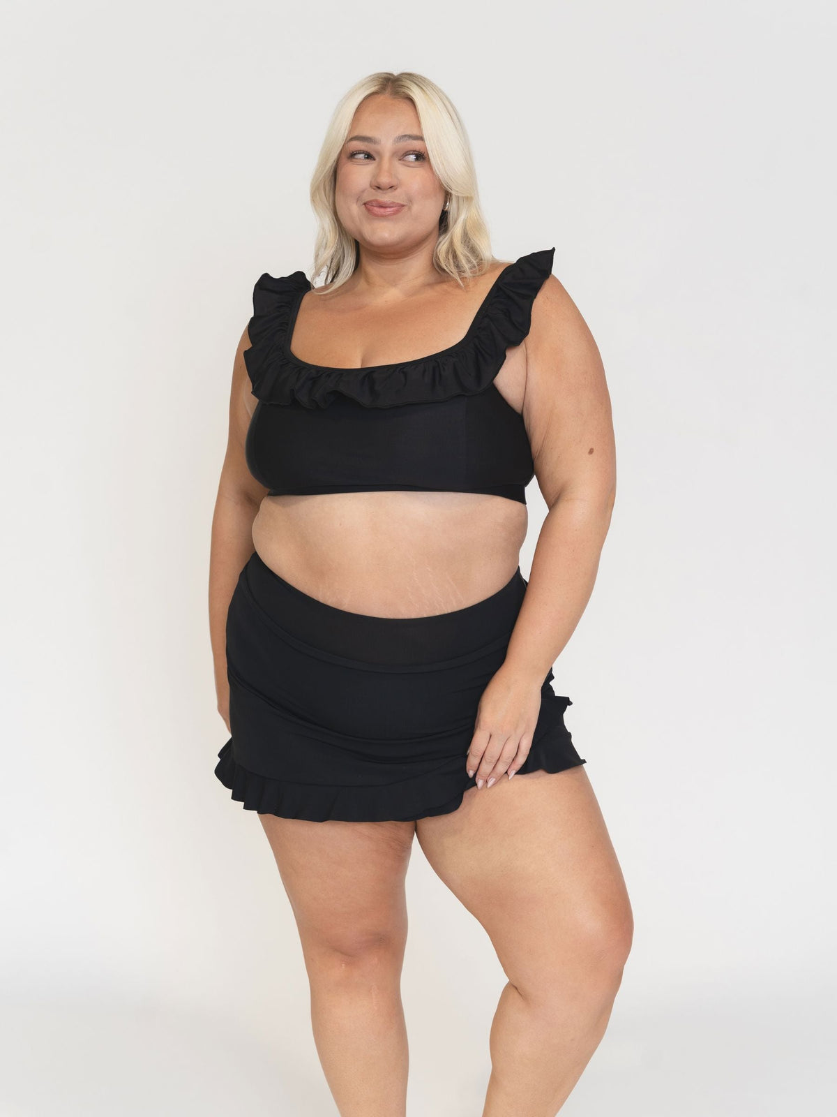 Woman wearing a black ruffled swimsuit against a white background