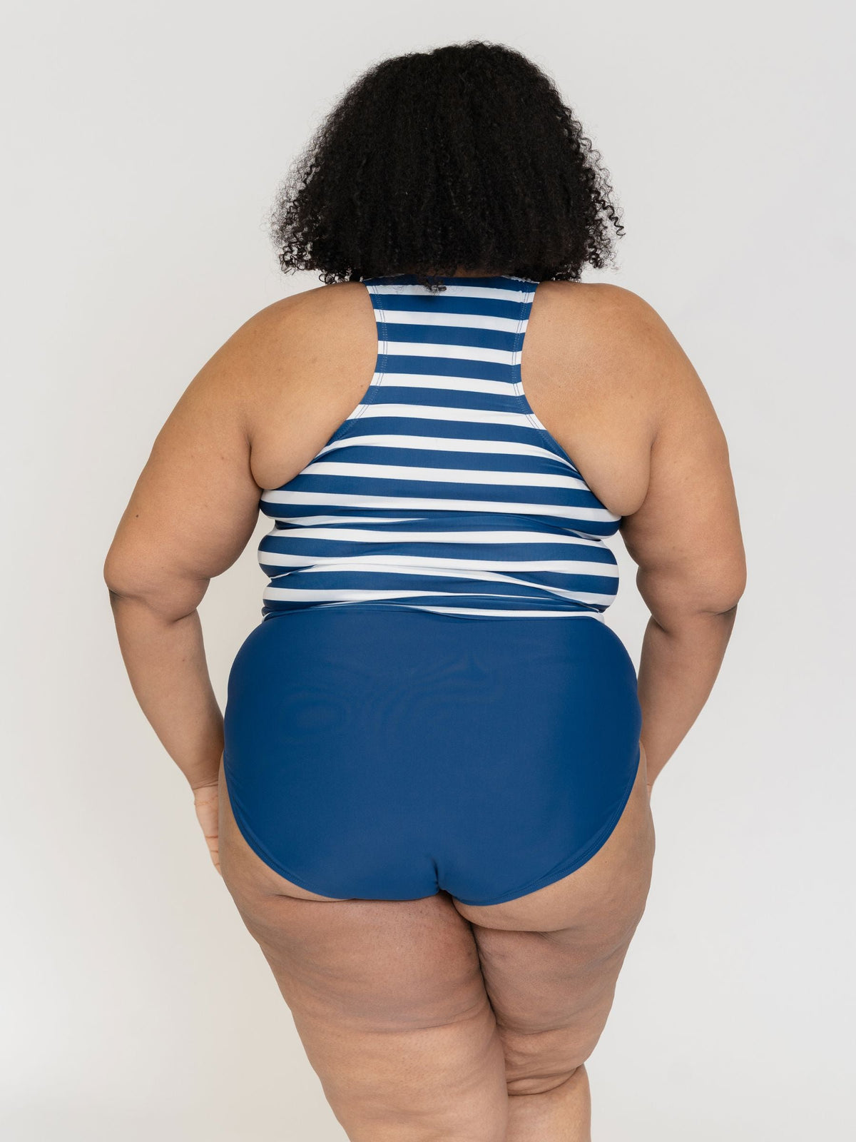 Person wearing a blue and white striped tank top and blue high-waisted shorts on a plain background