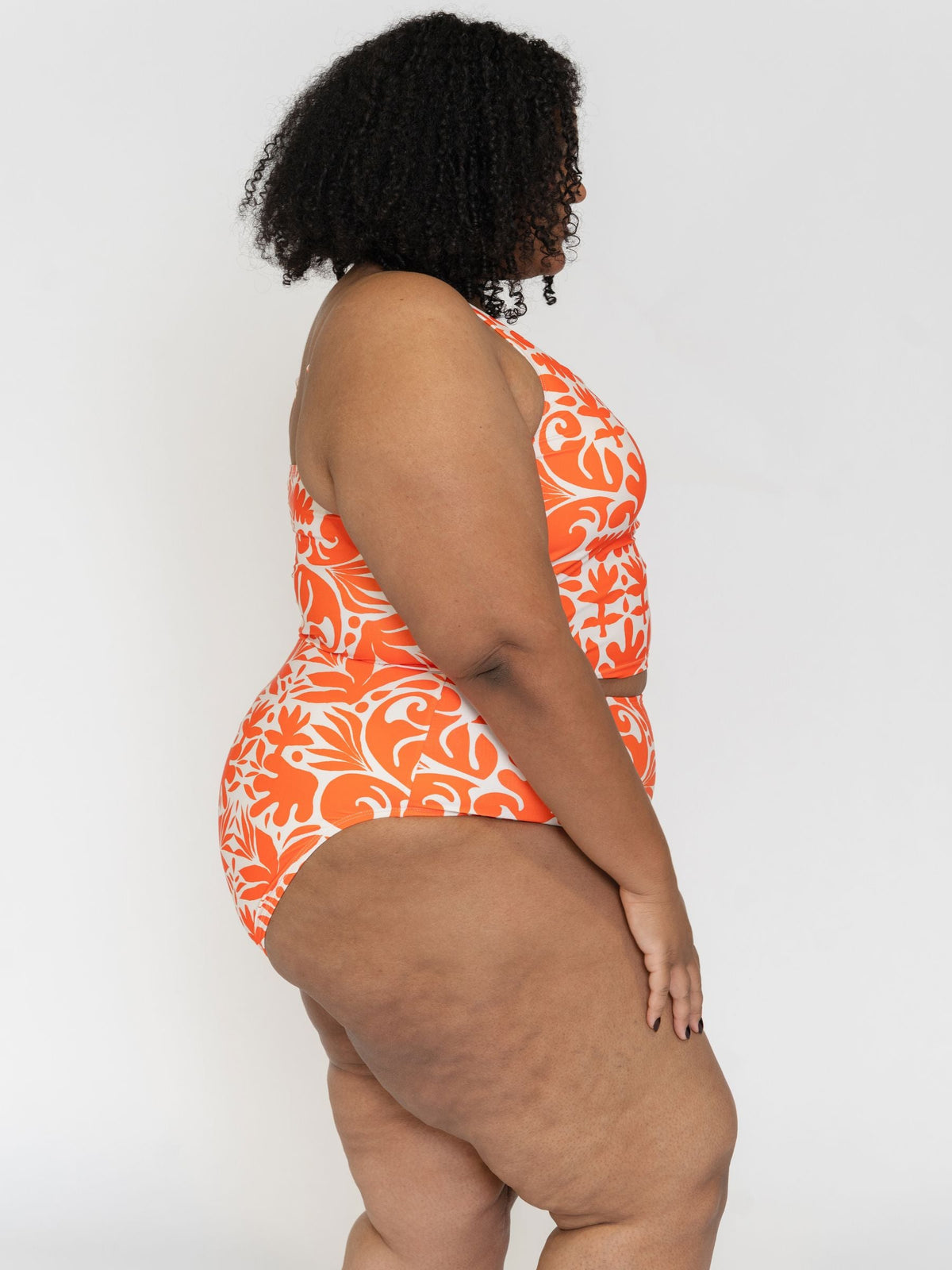 Person wearing an orange and white patterned swimsuit on a plain background