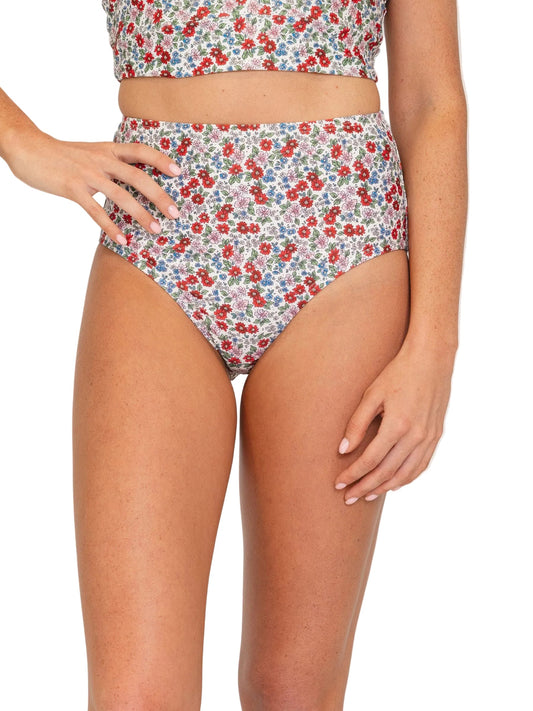 A model wearing a two-piece bikini set with a dense red, blue, and yellow floral print on a white background, shown from the chest down against a plain white studio background.