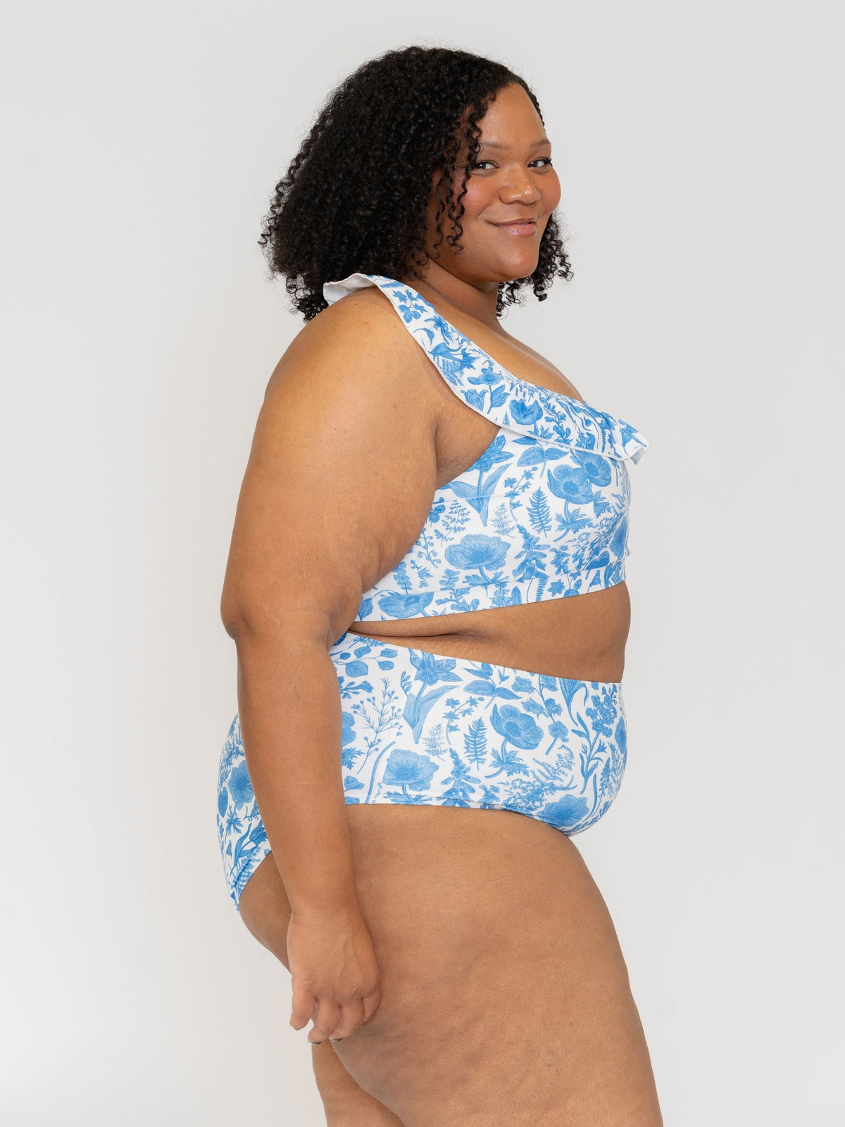Woman wearing a blue floral one-shoulder swimsuit against a white background