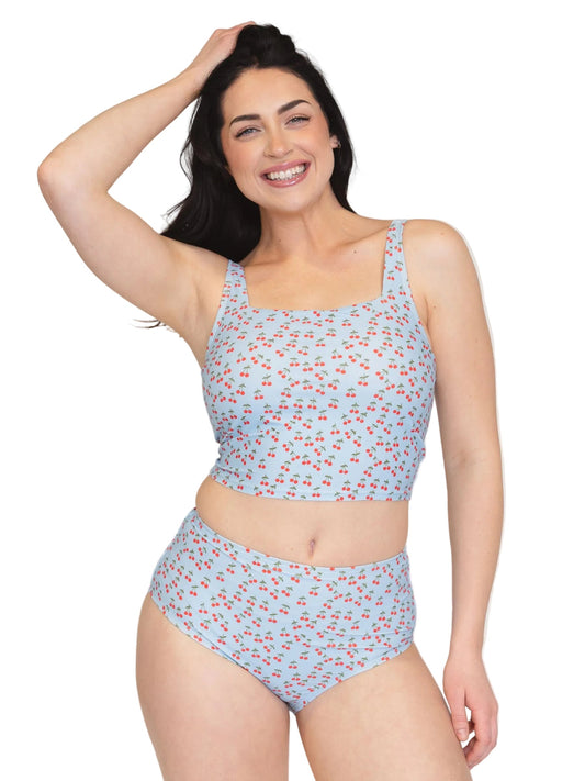 A woman modeling a two-piece swimsuit with a light blue base and a small red cherry print, set against a plain white background.