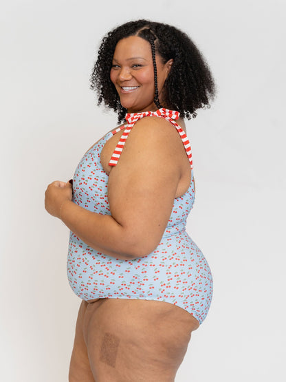 Woman wearing a blue floral swimsuit with a red and white striped tie on a plain background