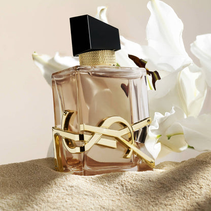 Yves Saint Laurent Libre Flowers & Flames Eau de Parfum bottle on a beige surface with white flowers in the background