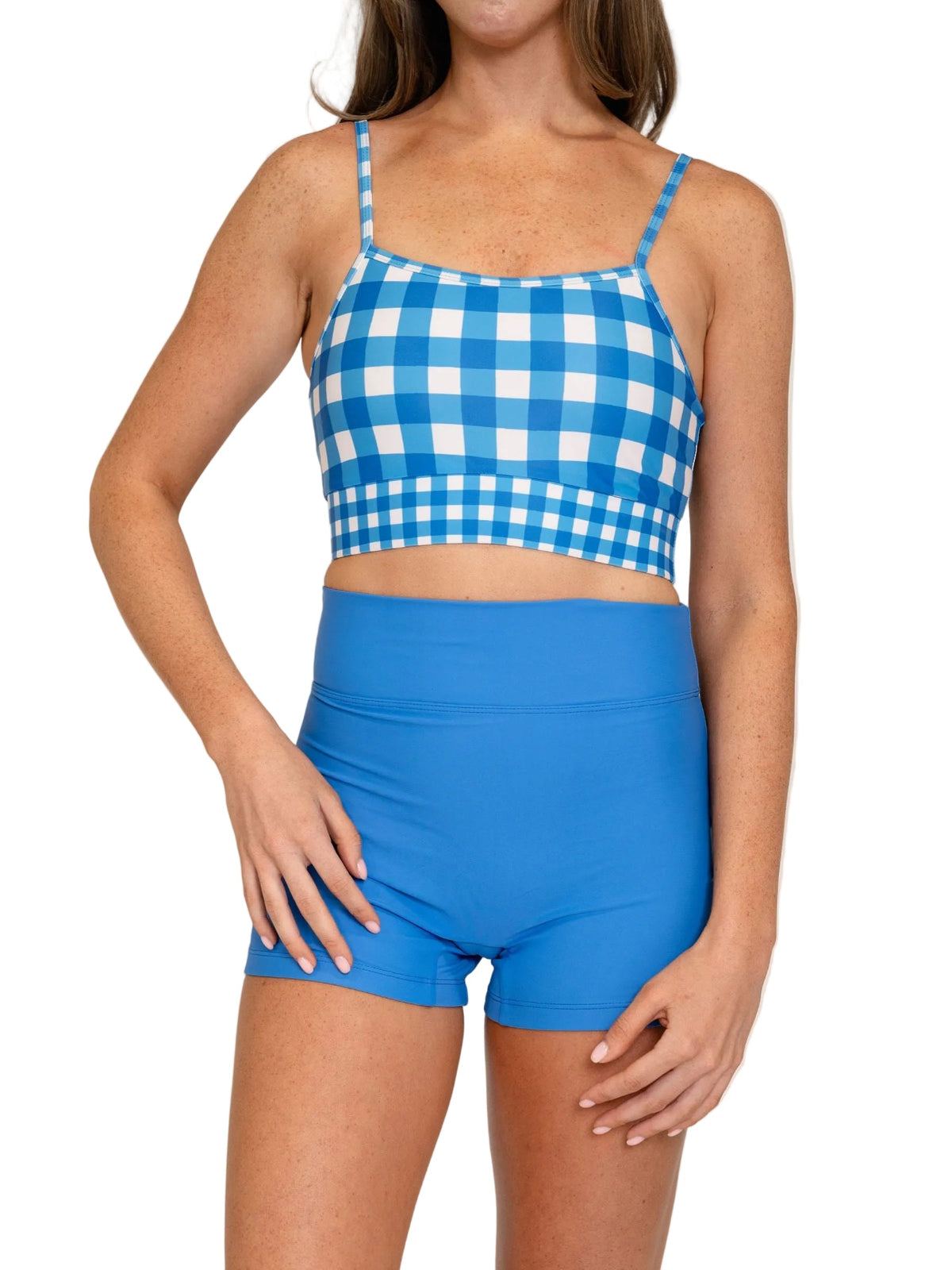 A model wearing a two-piece swimsuit featuring a blue and white gingham check crop top with thin straps and solid blue high-waisted shorts, set against a plain white background.
