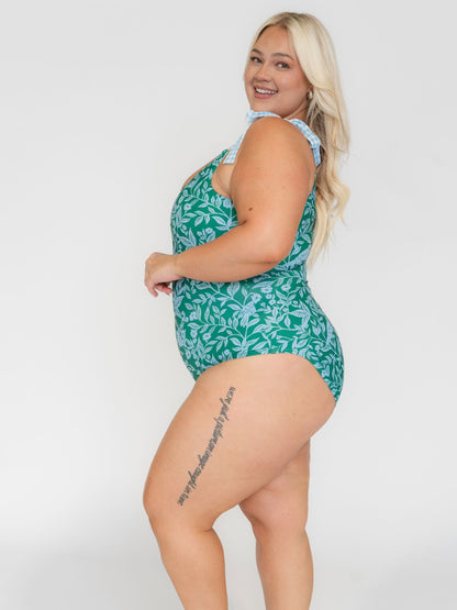 Woman wearing a green leaf-patterned swimsuit on a white background