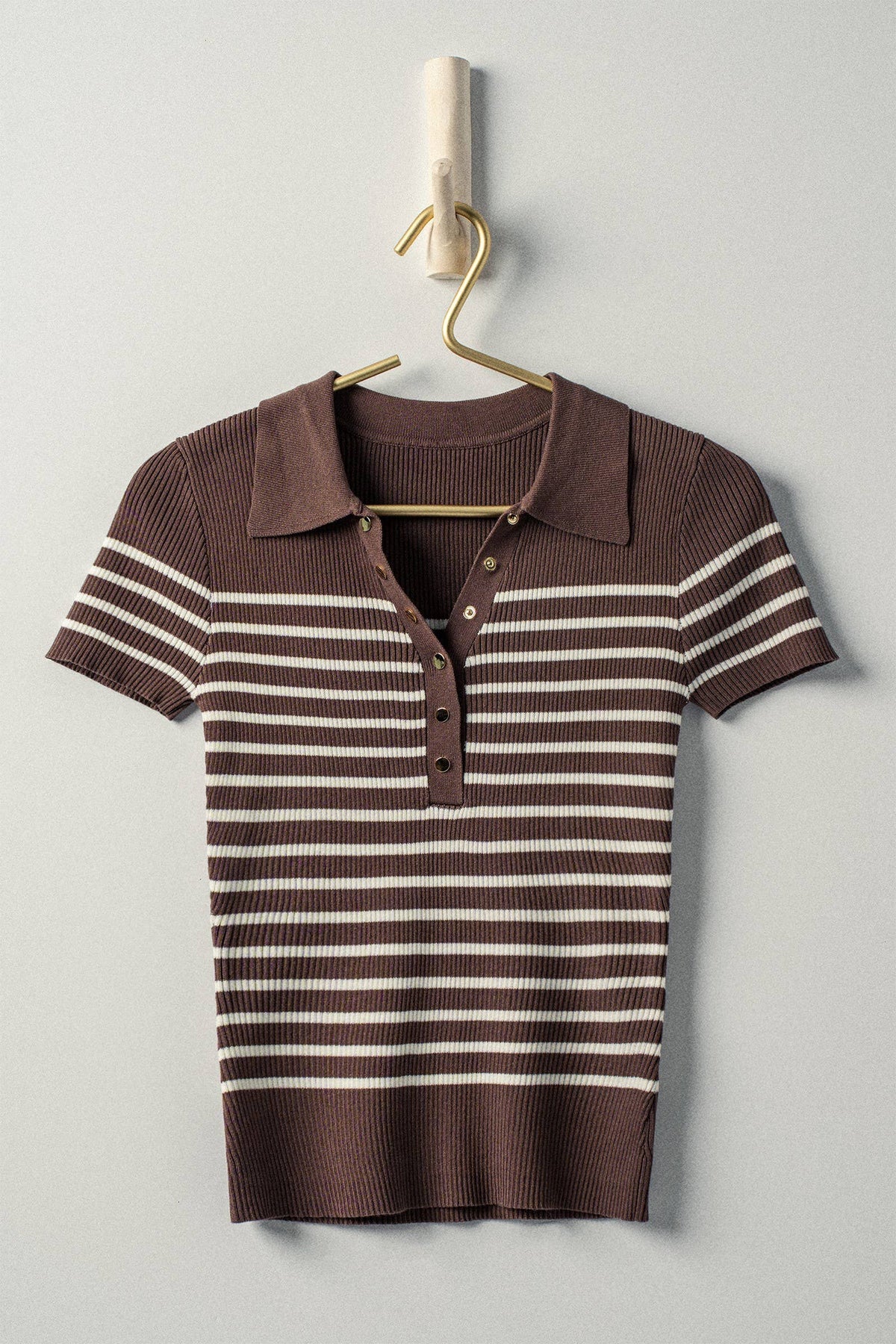 Brown and white striped polo shirt on a hanger against a light gray background