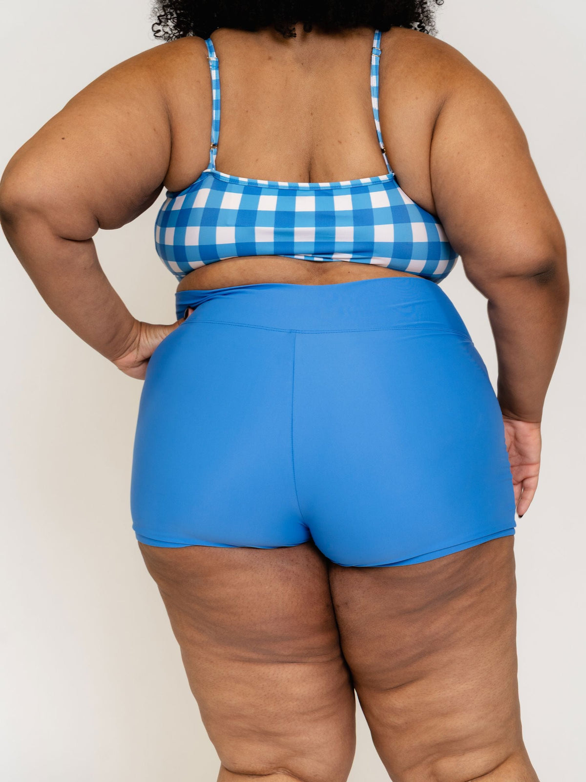 Person wearing a blue and white checkered top and blue shorts on a plain background