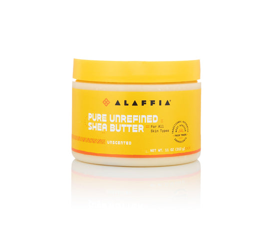 A yellow jar of Alaffia Pure Unrefined Shea Butter, unscented, on a white background with a soft reflection underneath