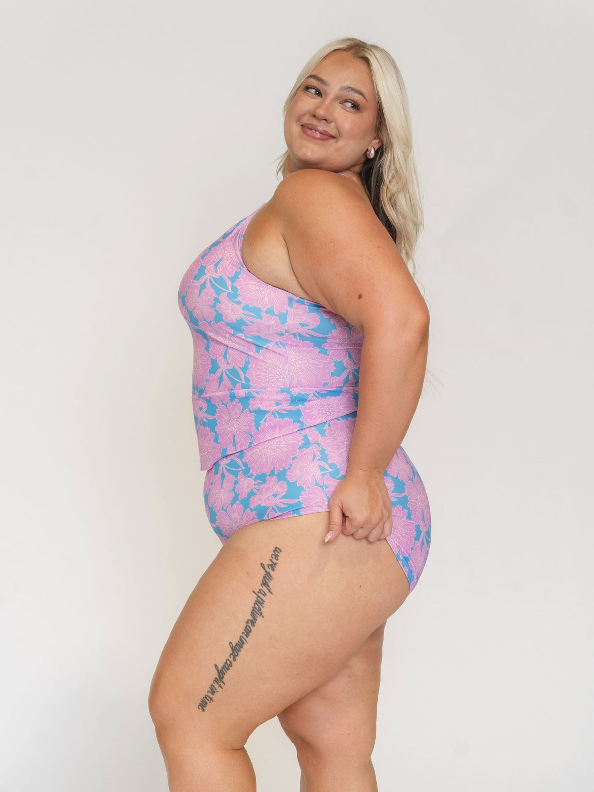 Woman wearing a pink and blue floral one-piece swimsuit on a white background