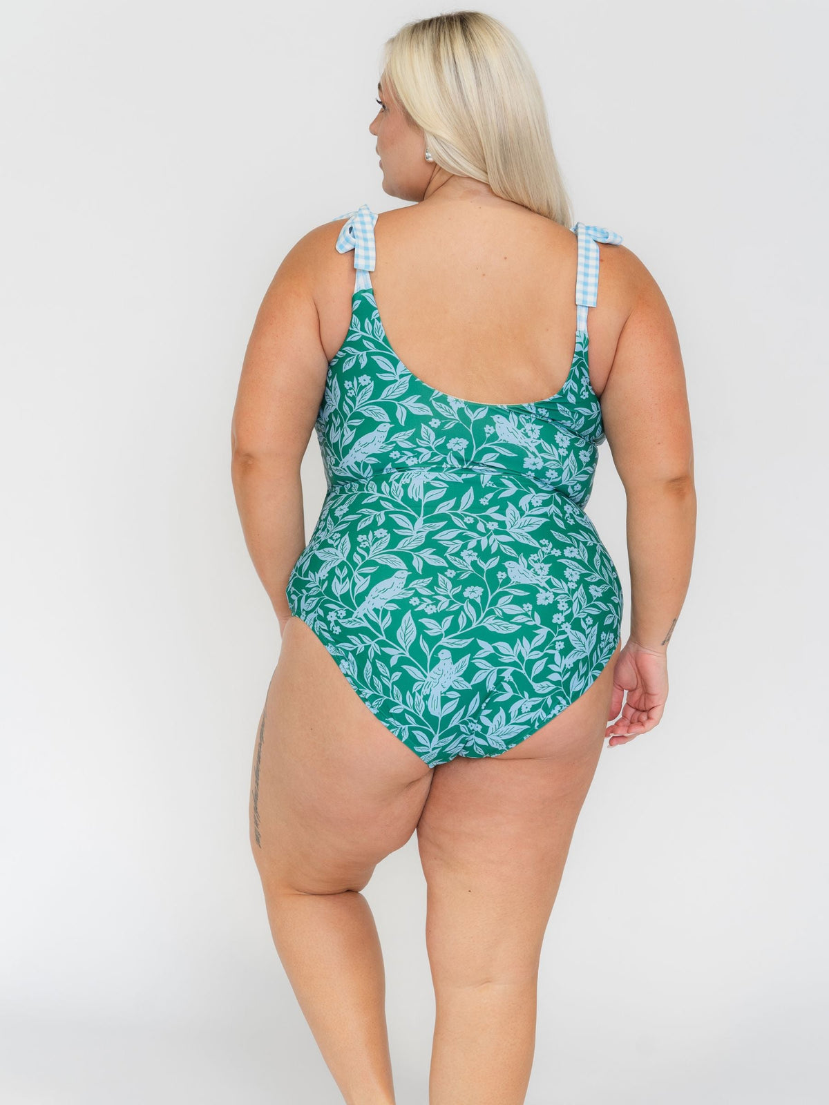 Woman wearing a green leaf-patterned swimsuit on a white background