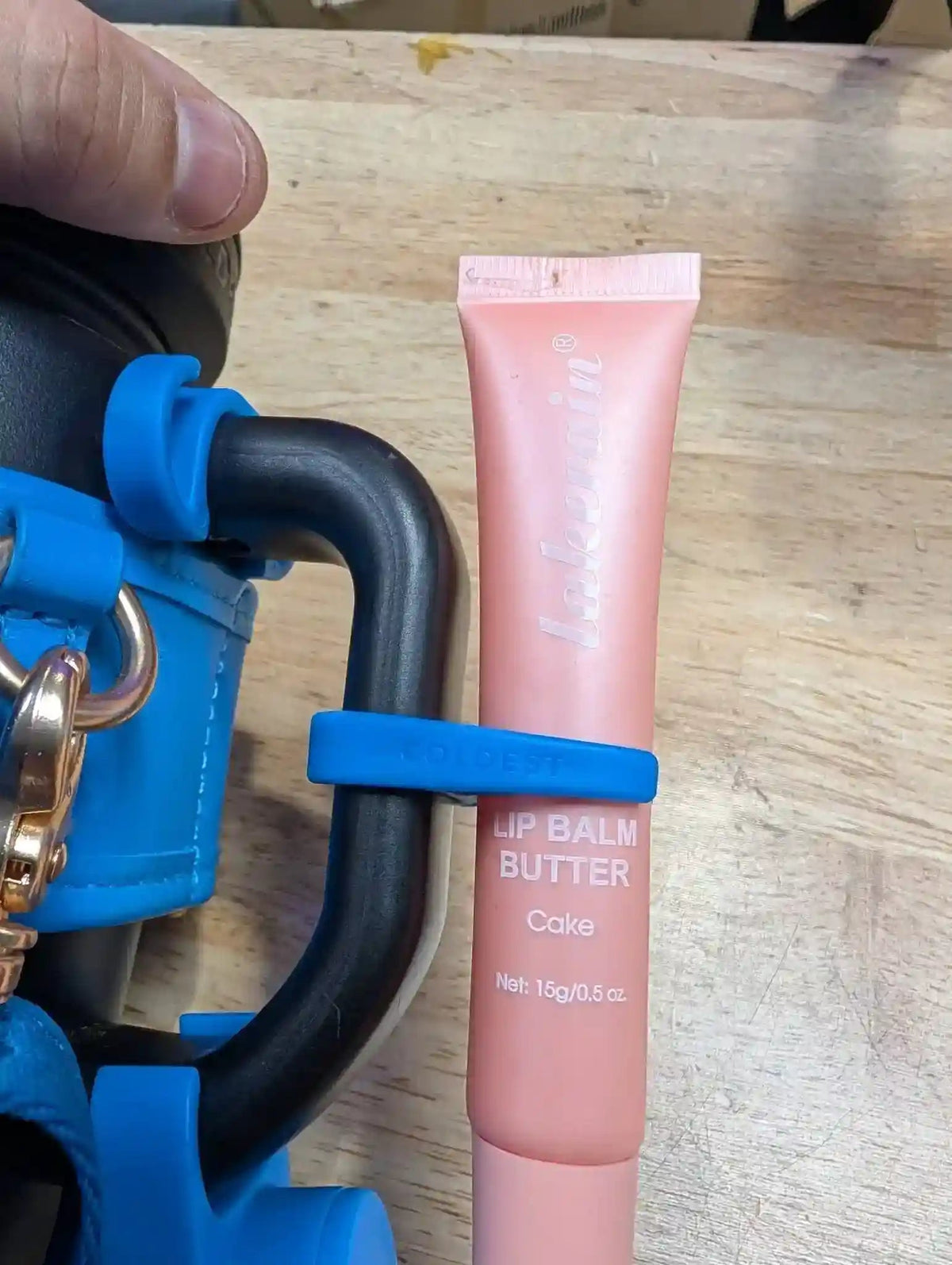 Pink lip balm tube with blue applicator on a wooden surface