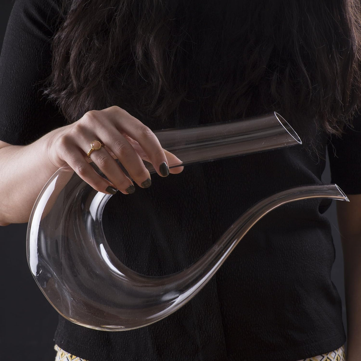 Person holding a clear glass vase with a long neck and wide base against a dark background