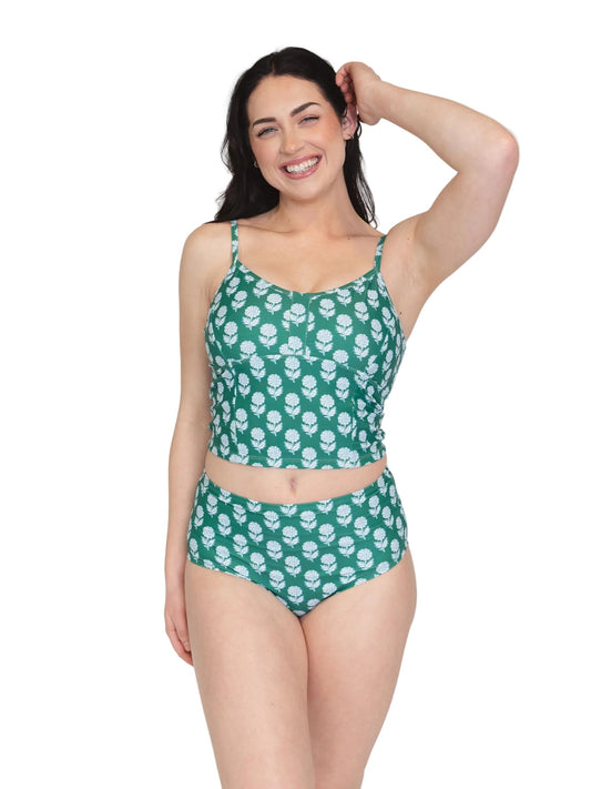 A woman modeling a two-piece swimsuit with a green base and white floral pattern, featuring a spaghetti-strap crop top and high-waisted bottoms, against a plain white background.