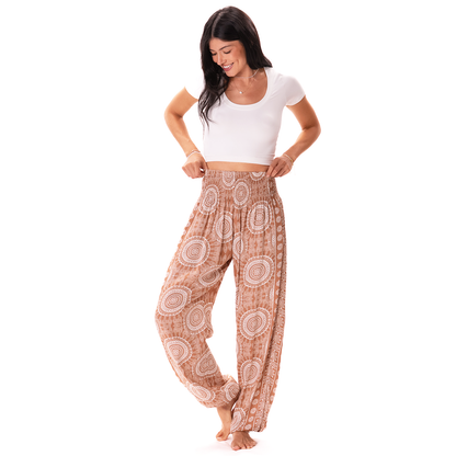 A woman modeling high-waisted, loose harem-style pants with a brown and beige paisley pattern, paired with a white crop top, on a solid white background.