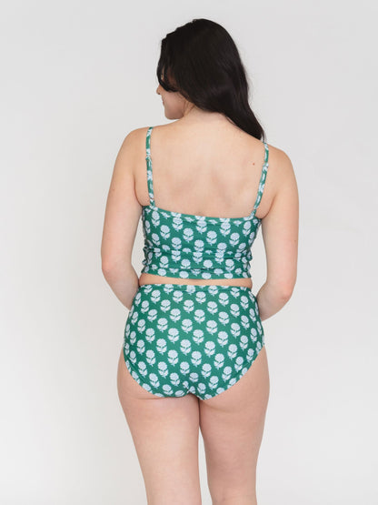 Woman wearing a green and white patterned swimsuit on a plain background