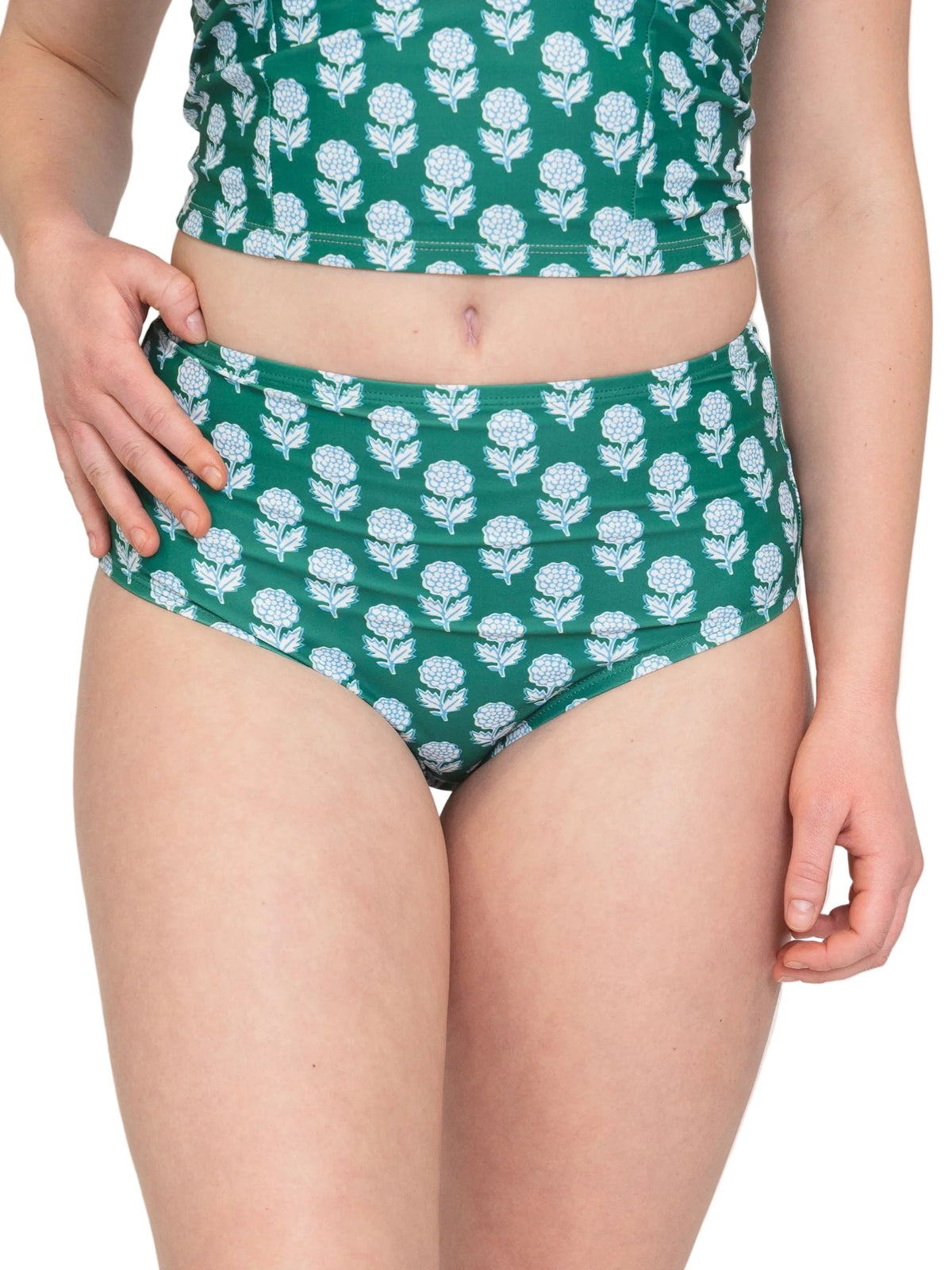 A model wearing a two-piece swimsuit with a green base and a white floral block print pattern, featuring a high-waisted bikini bottom and a matching cropped top.
