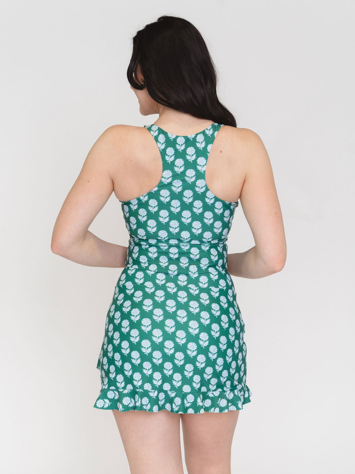 Woman wearing a green dress with white floral pattern on a plain background