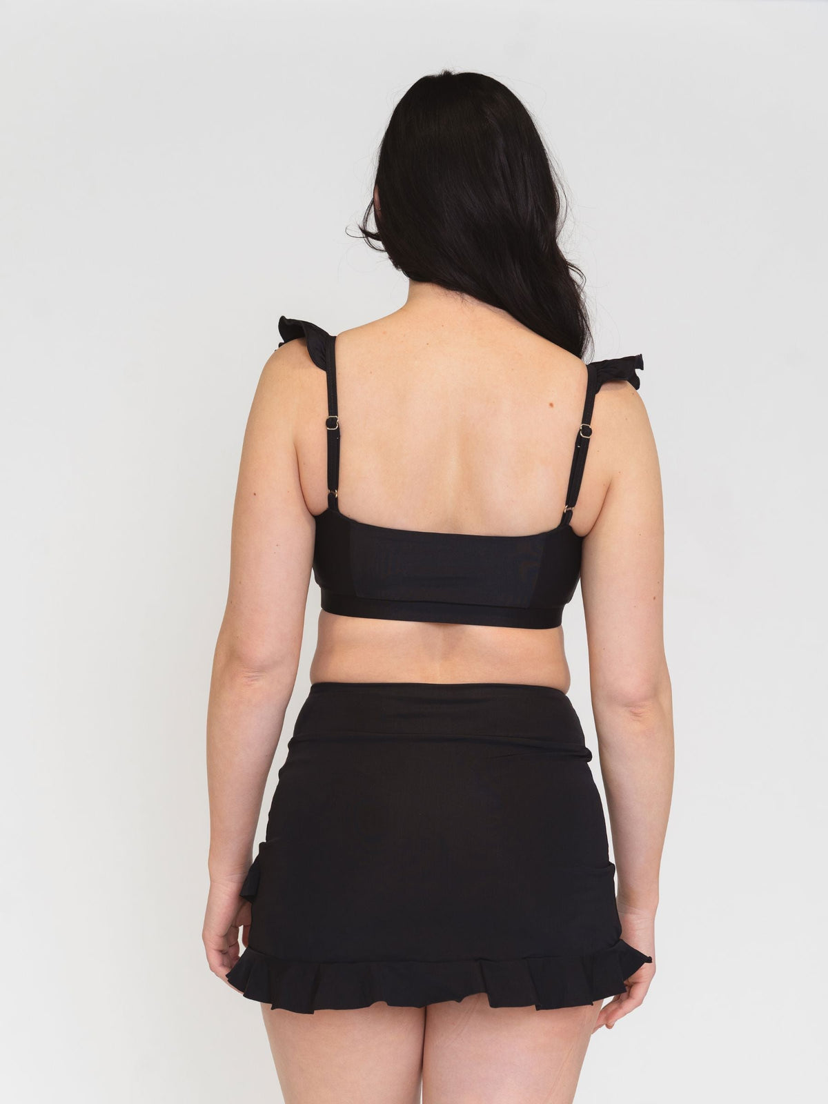 Person wearing a black bikini set with ruffled straps on a white background