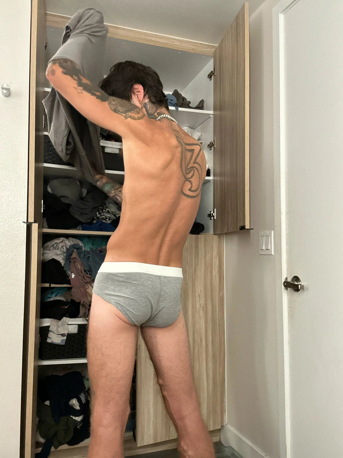Person wearing gray underwear standing in front of an open closet.
