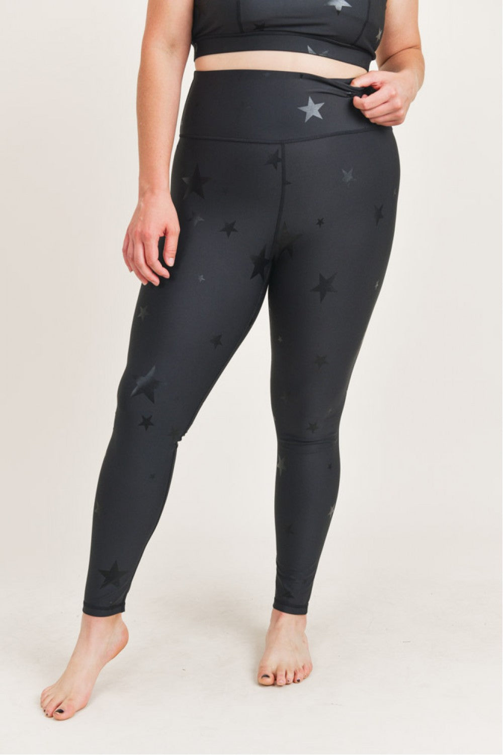 Person wearing black leggings with star patterns on a plain background