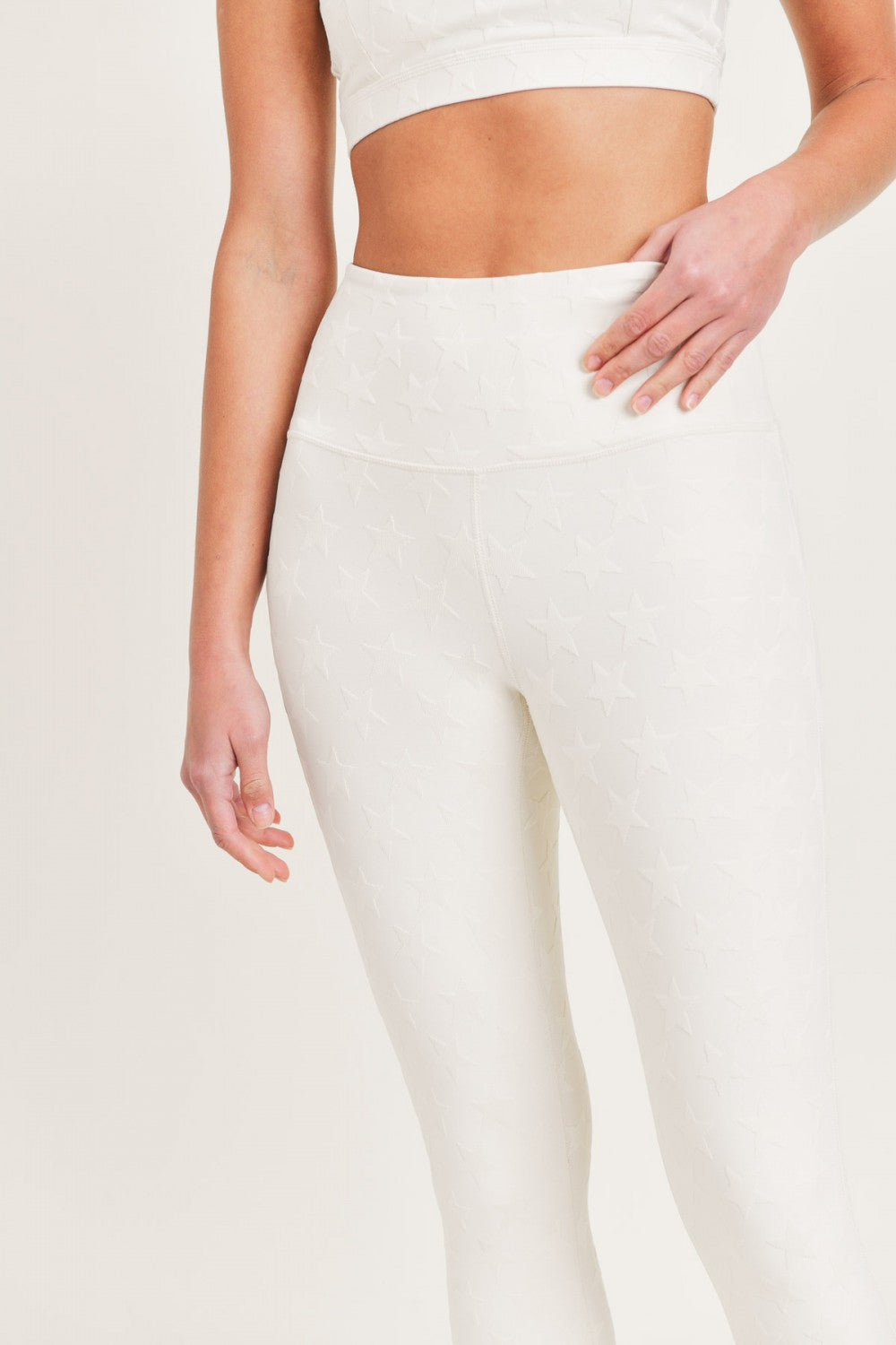 Person wearing white leggings and a cropped top on a plain background