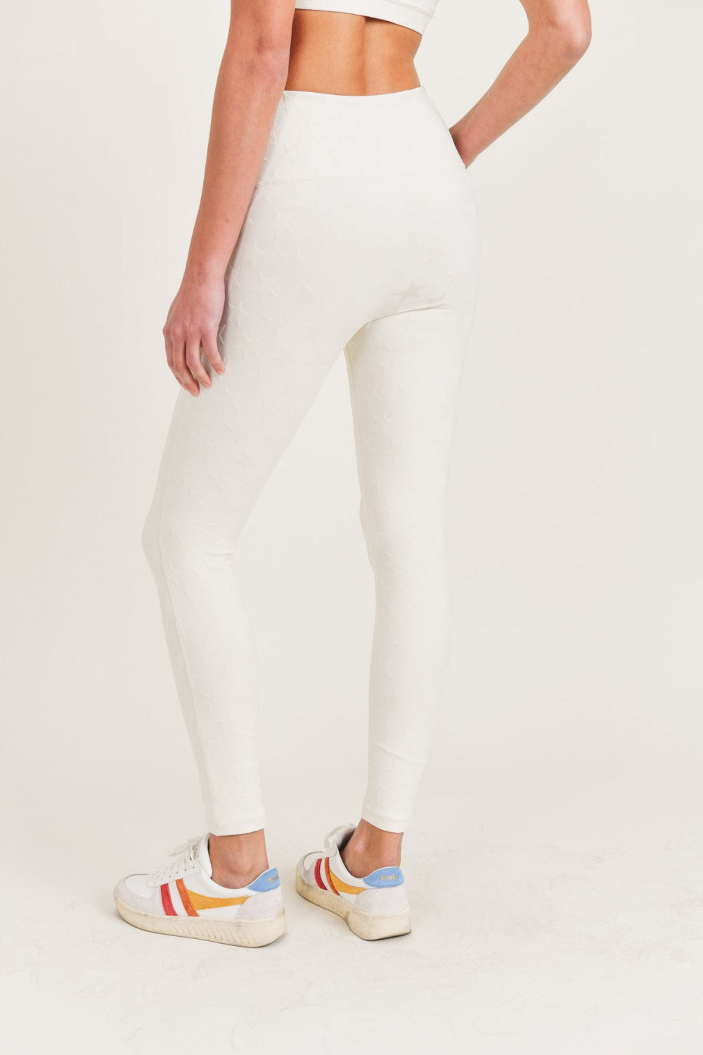 Person wearing white leggings with colorful sneakers on a light background